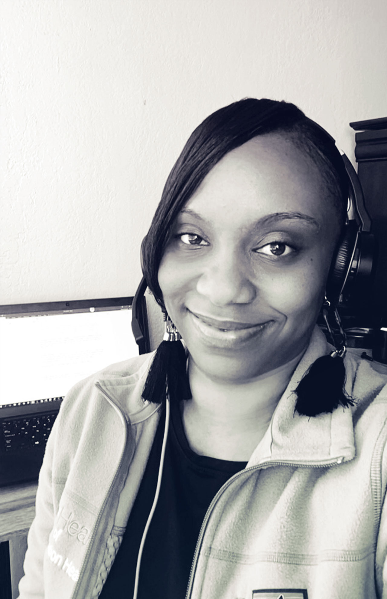 Portrait of Monique Posey with her headset on and computer in the background.
