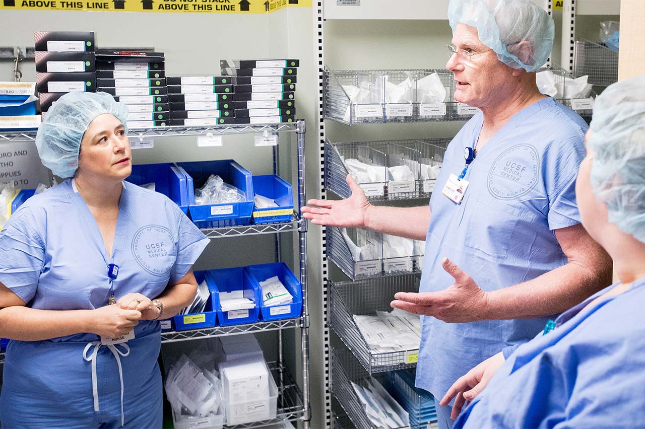 Photo of doctors in scrubs in a supply room in a hospital having a discussion.
