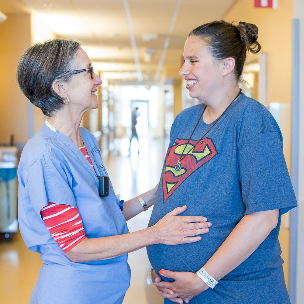 A doctor and her pregnant patient laugh together while the doctor places her hands on the patient's stomach