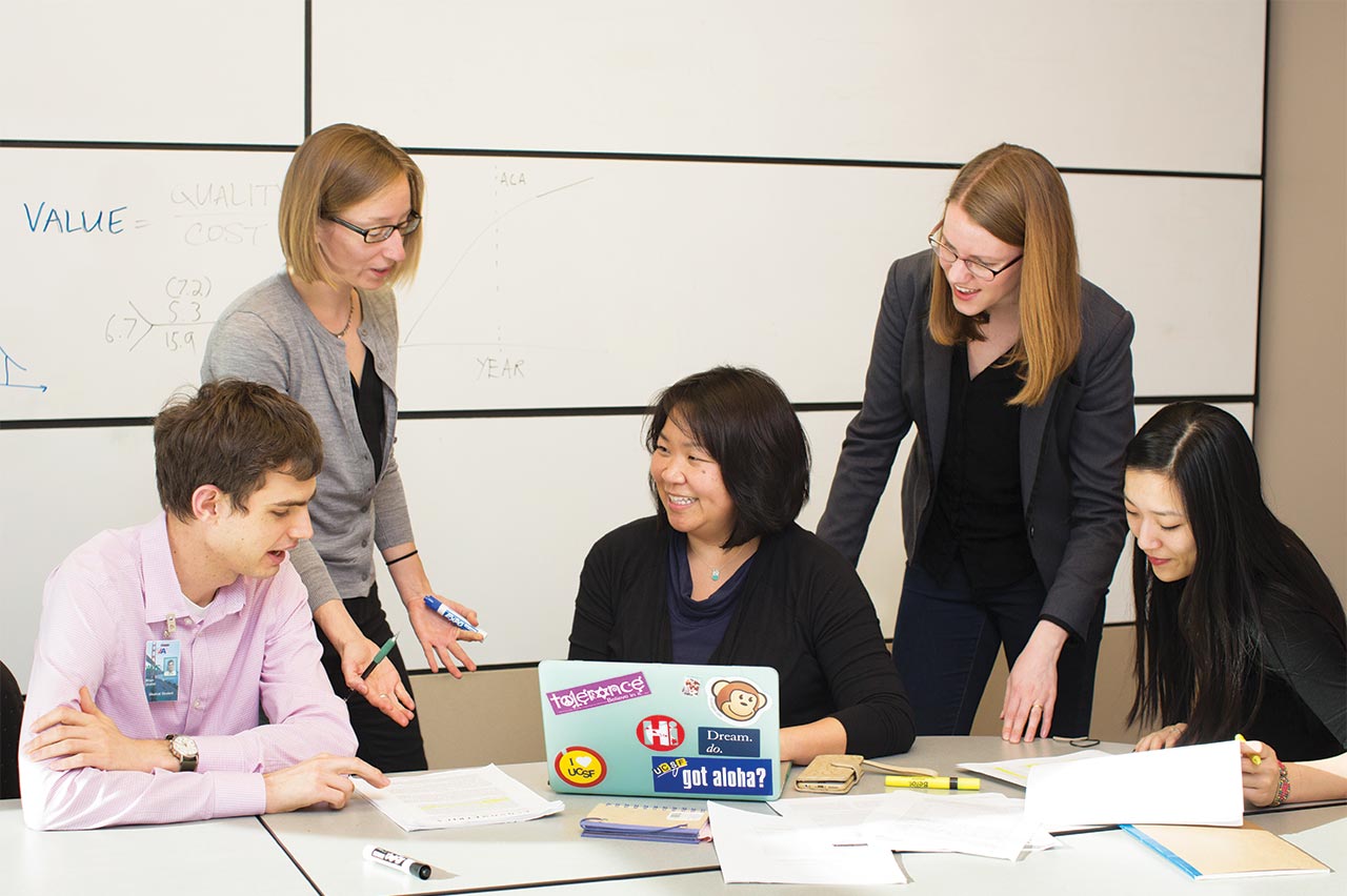 A group of people having a discussion around a table with papers and a laptop.