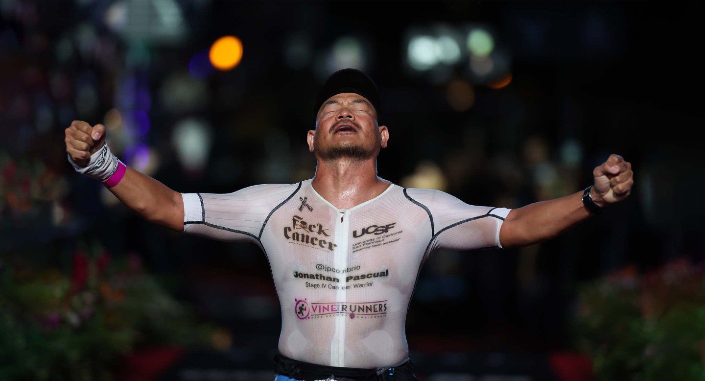 Jonathan Pascual crosses the finish line at the 2024 VinFast IRONMAN World Championship with his arms in the air and his head looking up in relief and triumph.