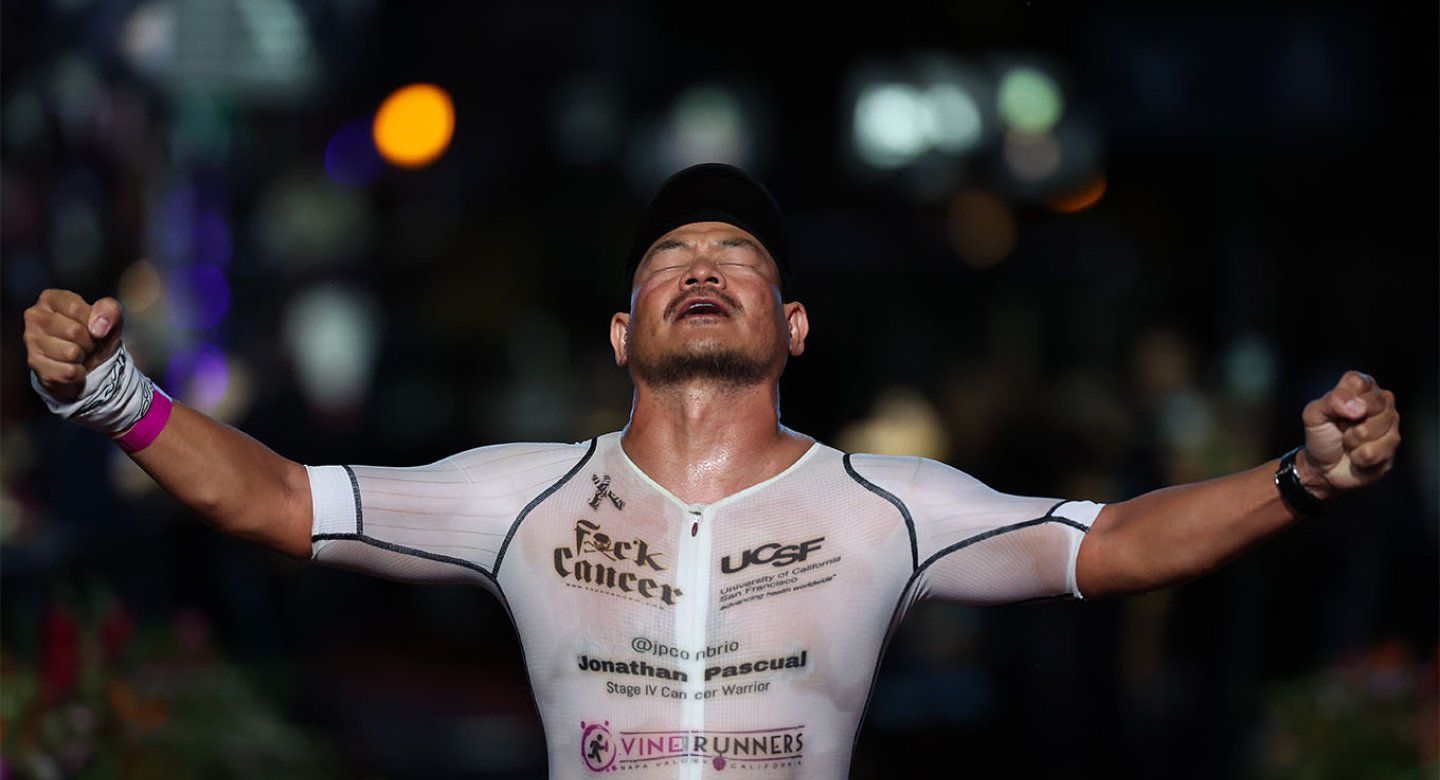 Jonathan Pascual crosses the finish line at the 2024 VinFast IRONMAN World Championship with his arms in the air and his head looking up in relief and triumph.