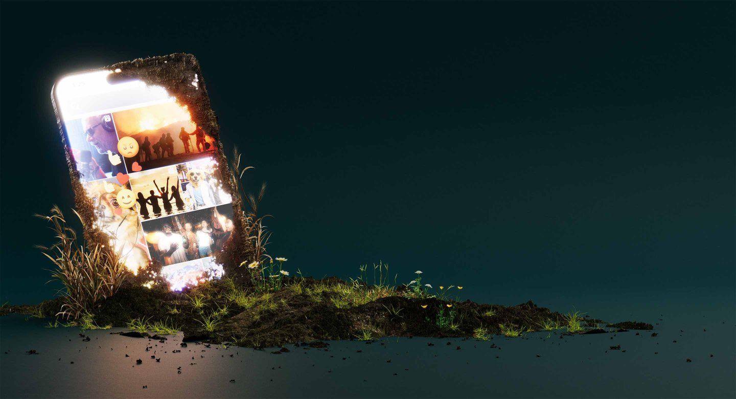 A large smartphone, partially buried in soil, is set against a dark background, with a brightly lit screen showing multiple images: people celebrating and dancing, dog memes and photos, a wildfire, and a podcaster, along with thumbs-up, heart, smiley face, and angry face emojis.