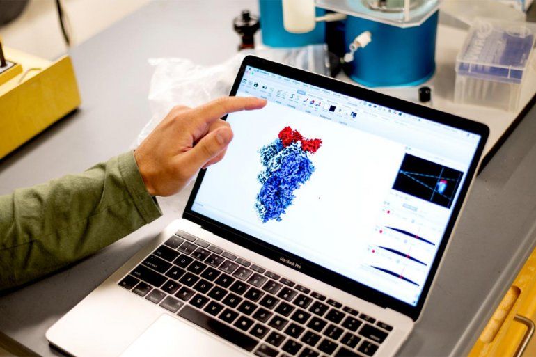 A hand points to a laptop computer screen with a cryo-electron image of a nanoprotein.