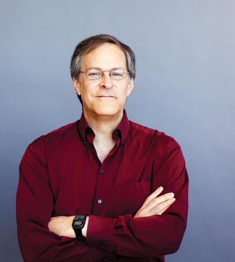 Portrait of Matthew Springer, standing with his arms crossed in front of an all grey background.