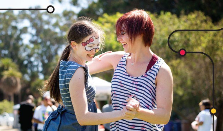 Two young girls in face paint dance together in a park.