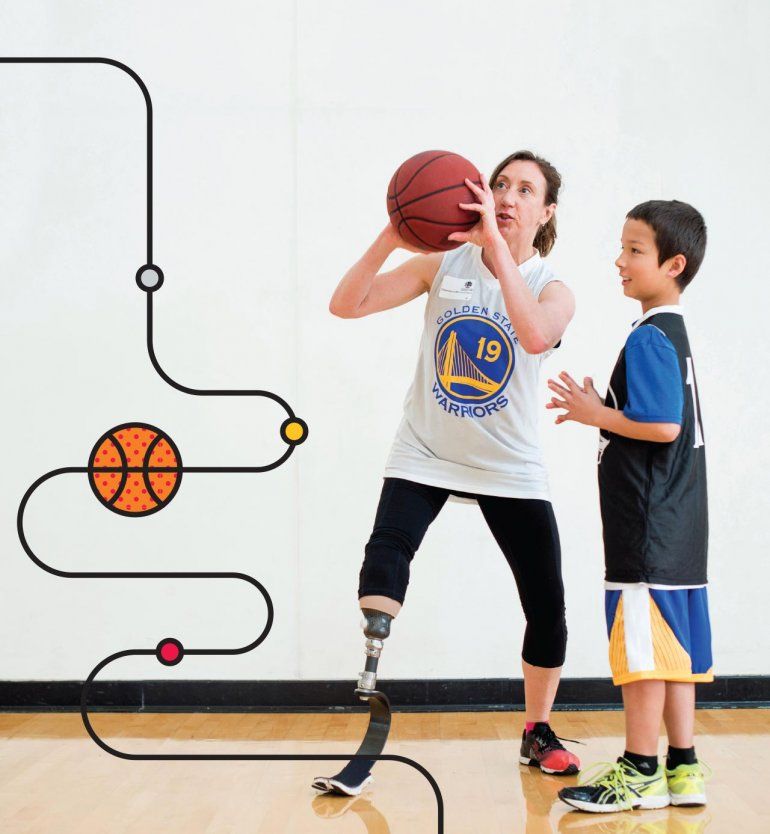 Debrah Bevilacqua (left), has a prosthetic leg from the knee down and wears a Golden State Warriors shirt, shows a young child (right) how to play basketball indoors.