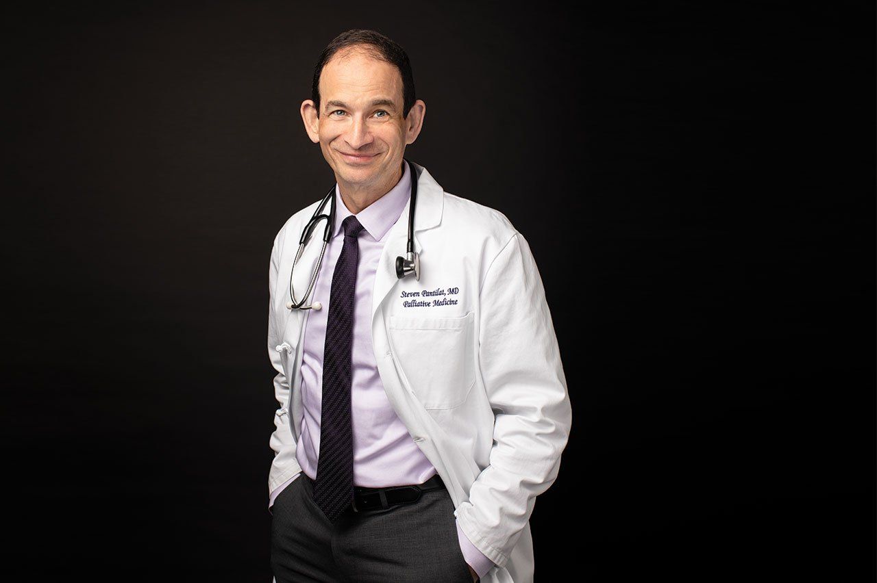 Photo of Steven Pantilat, MD, in a white doctor’s coat with a stethoscope draped around his neck, in front a black background. 