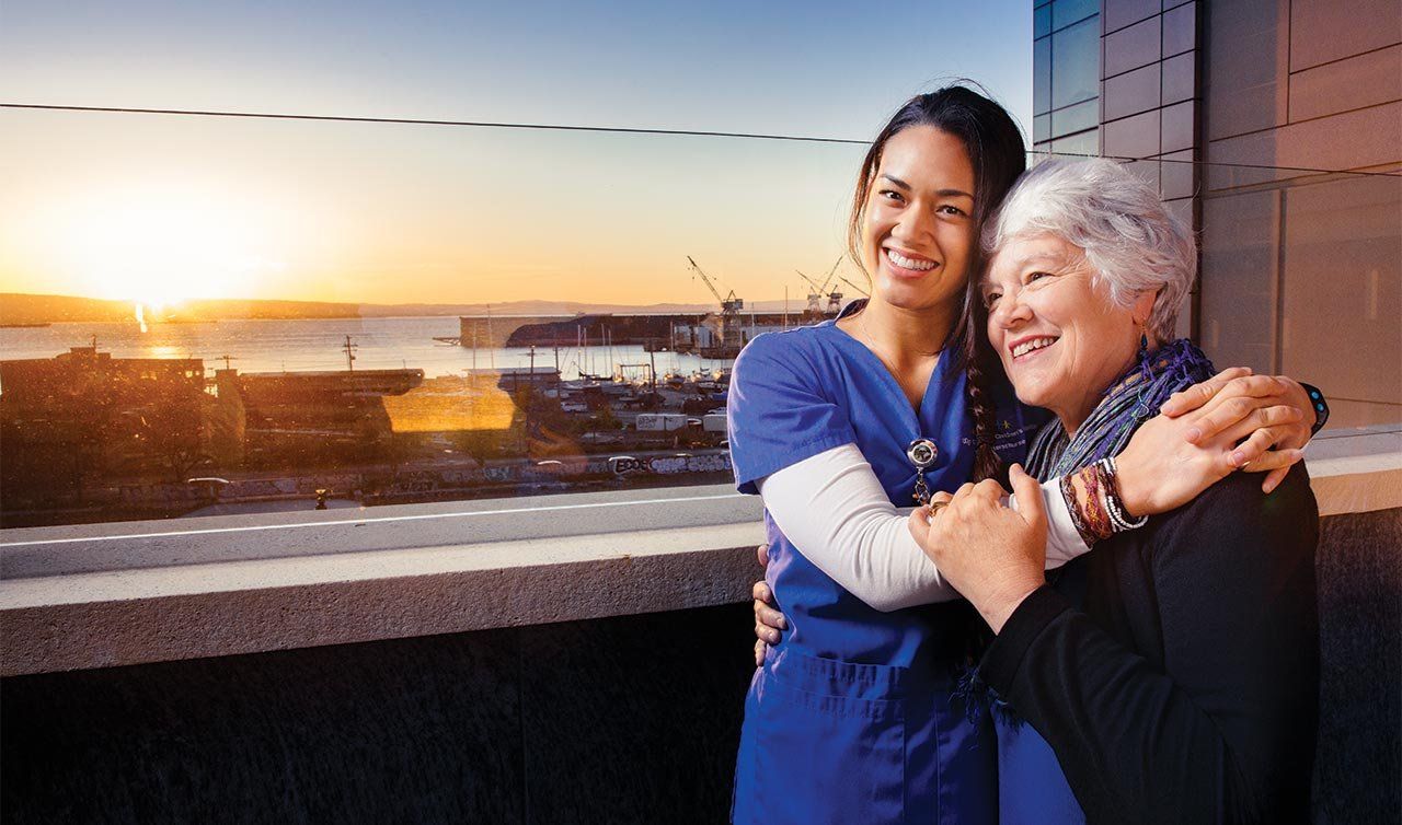 Photo of Mei-Ling Wong and Peggy Cadbury, embracing in a hug on the pediatric ICU roof garden of UCSF Benioff Children’s Hospital San Francisco at sunrise.