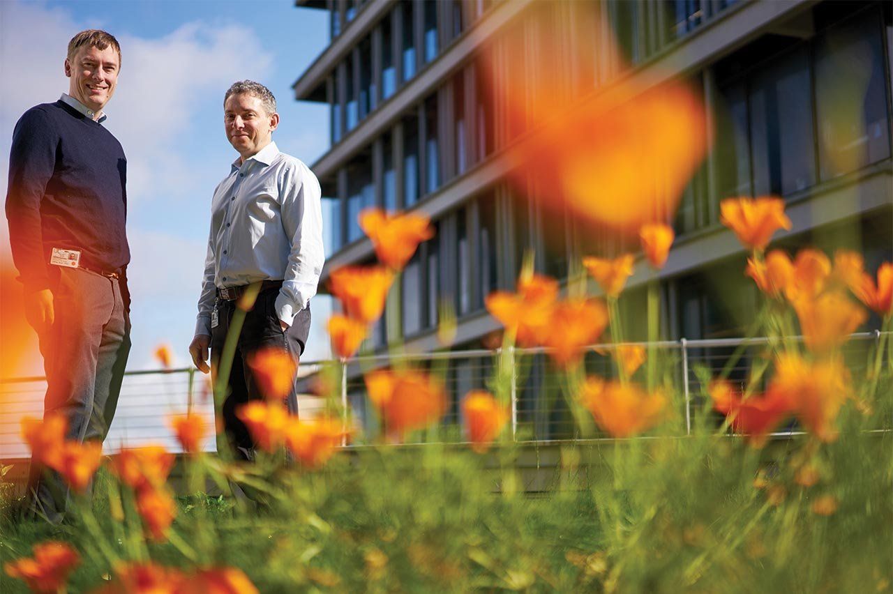 Ophir Klein and Jeffrey Bush stand outside by a bed of flowers