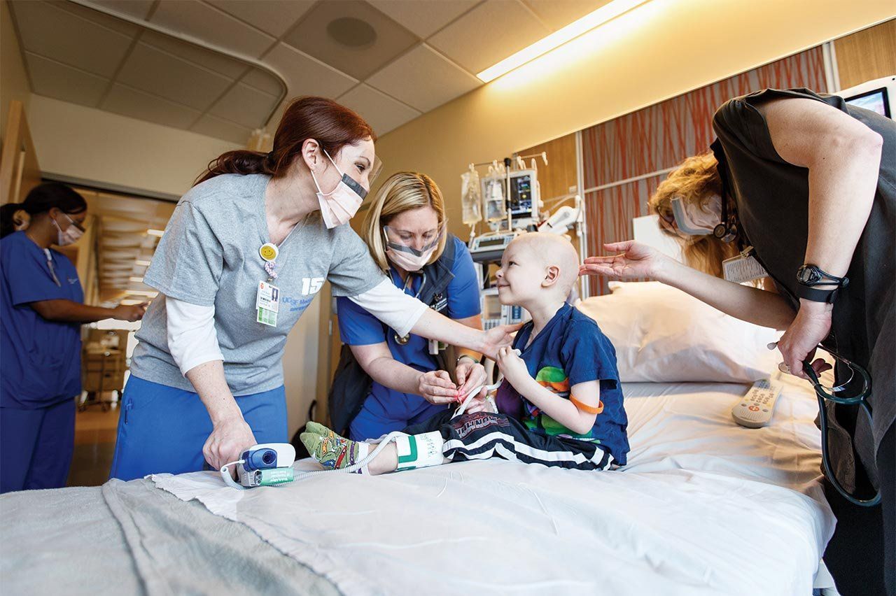 Nurses attend to a smiling child in a hospital bed.