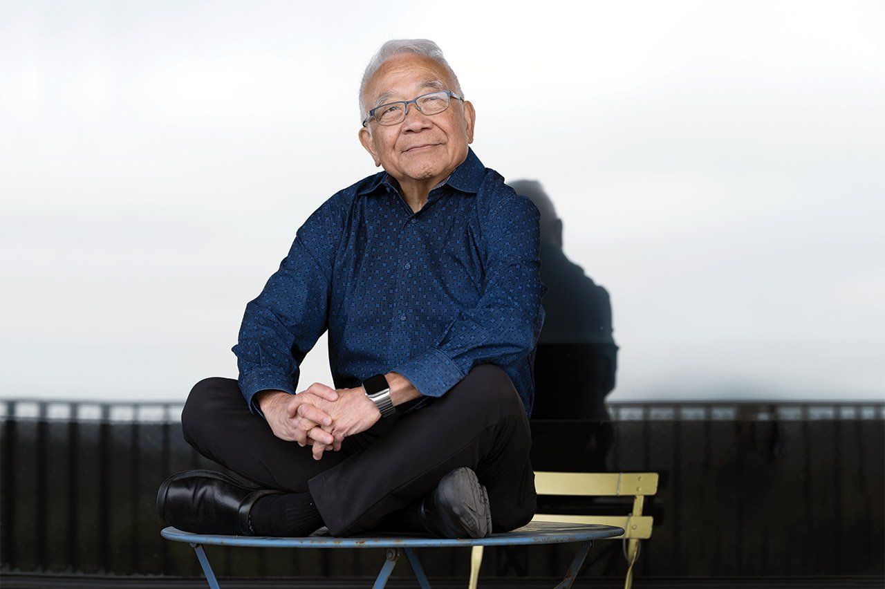Portrait of Keith Yamamoto, sitting cross-legged on a table.