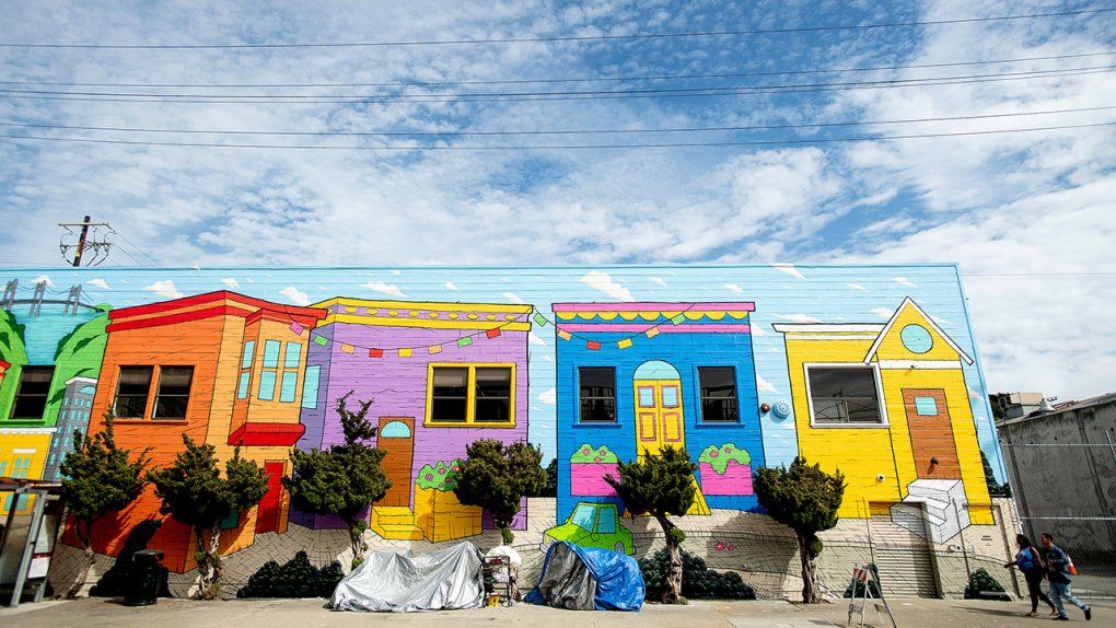 Homeless camp beside building with a mural of houses