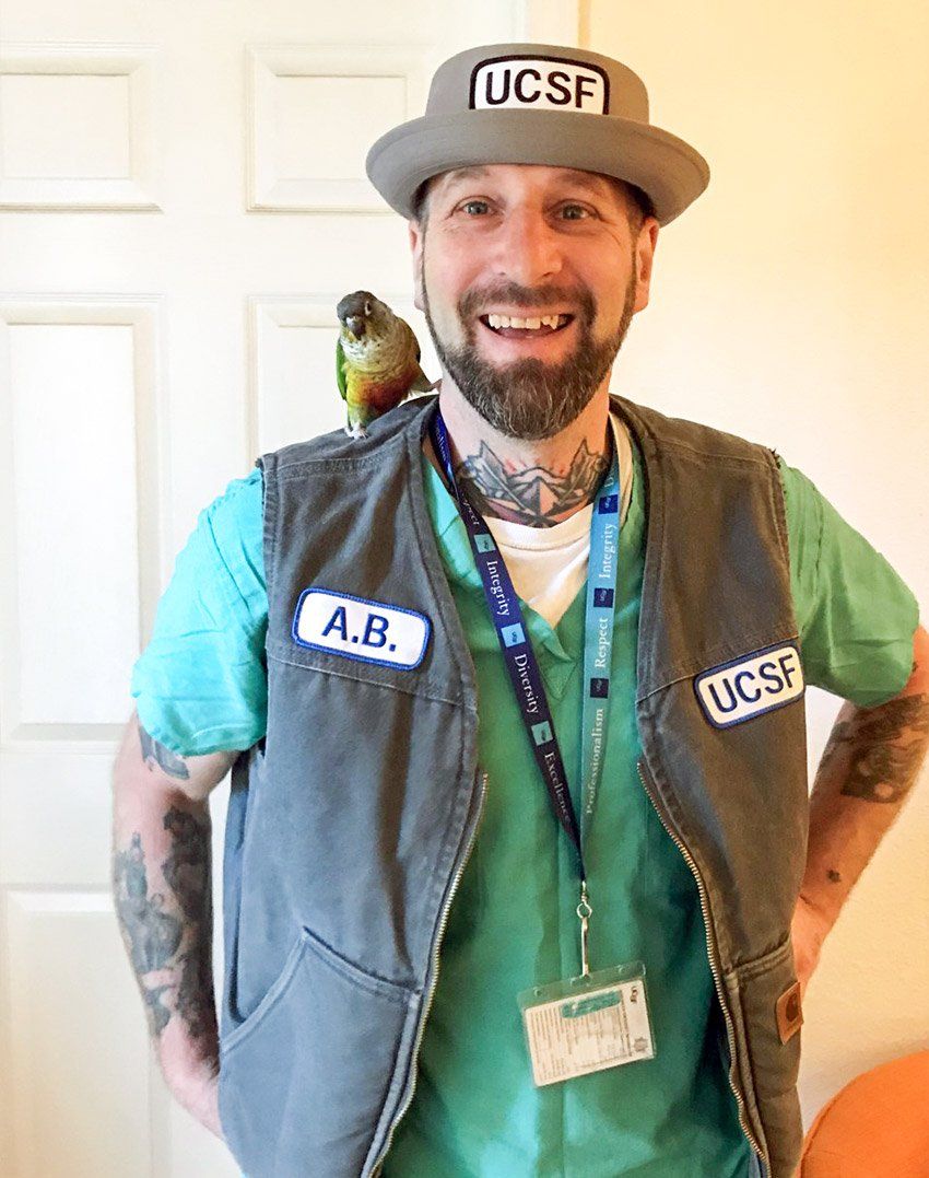 Abie Stillman at home in his UCSF hat and vest with his bird, Squeaky.