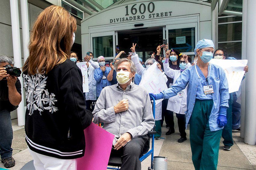 Kelly Timothy pushes patient Ronald Jay Temko in a wheelchair outside Mt. Zion hospital. He greets his wife among a crowd of supporters with signs.