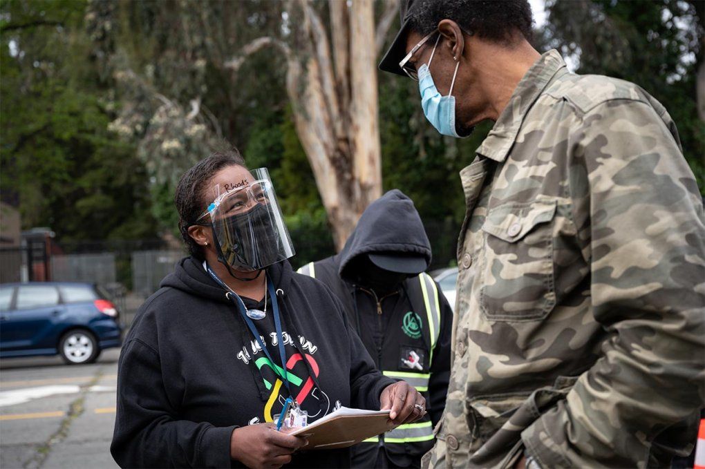 Photo of Kim Rhoads in a face mask and face shield talking to a man at a vaccine clinic.