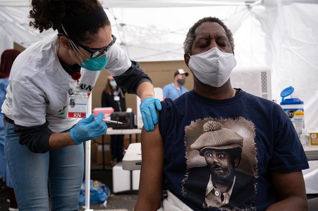 A Black man receiving a COVID-19 vaccine from a nurse at a community vaccine clinic.