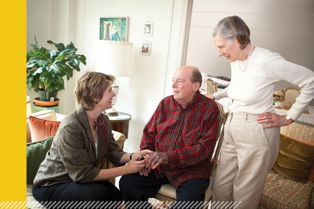 Dr. Rebecca Conant sits with an elderly male patient and an elderly woman stands behind him.