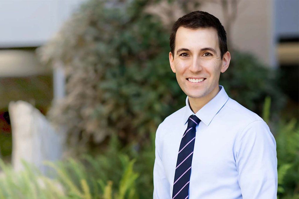 Christopher Abrecht stands in front of a building and greenery.