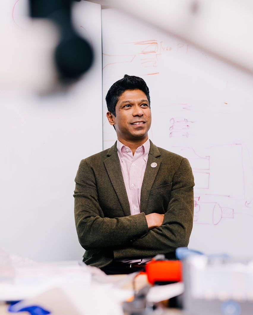 Prasad Shirvalkar stands with his arms crossed in front of a whiteboard with diagrams.
