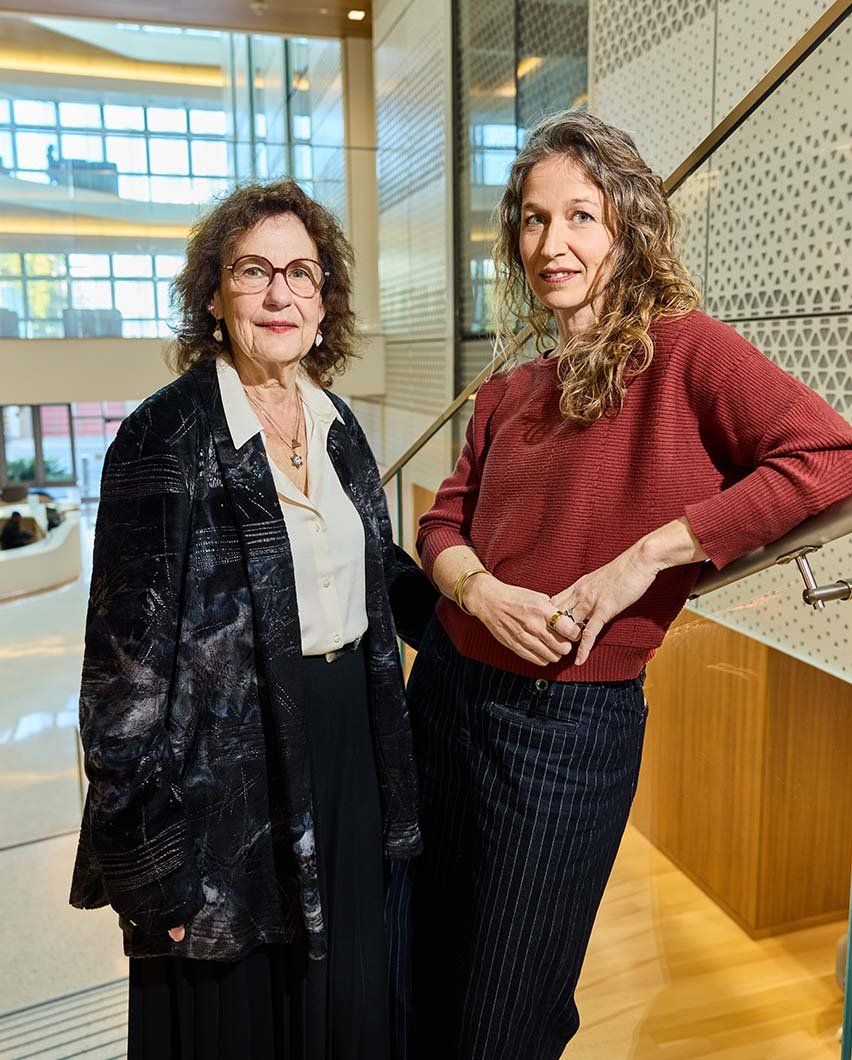 Alicia Lieberman and Nicki Bush stand on a stairway overlooking the light-filled atrium of the UCSF Nancy Friend Pritzker Psychiatry Building.