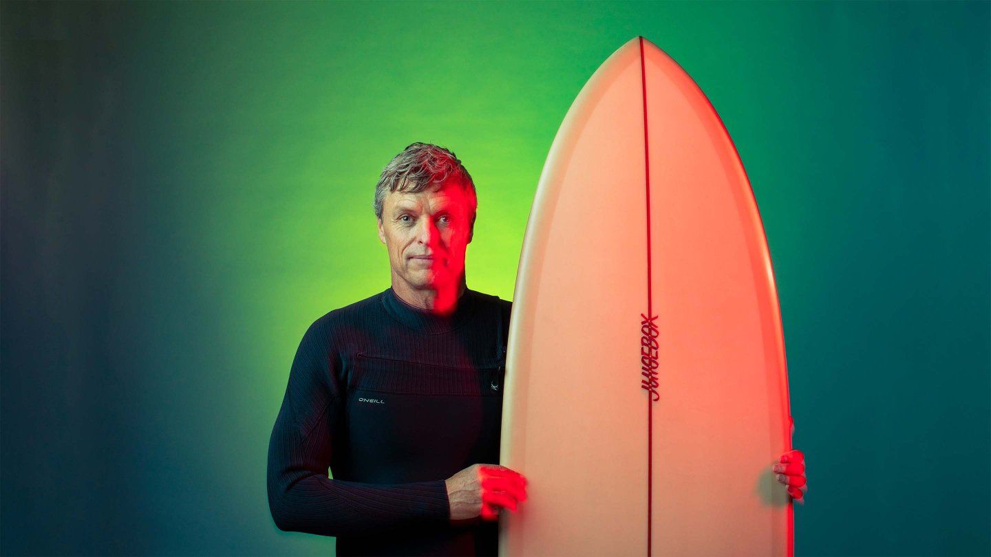 Thane Schultz stands with his surfboard.
