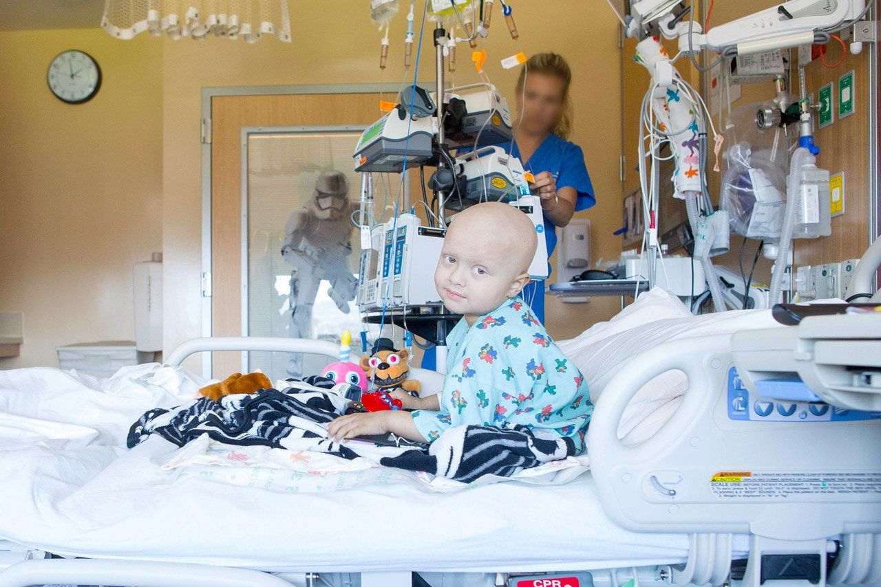 Kayson sits in his hospital bed as a nurse works in the background.