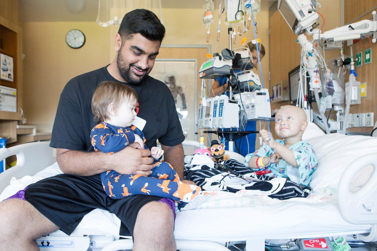 Kayson sits in his hospital bed with uncle Sukhi and baby brother Zyan.