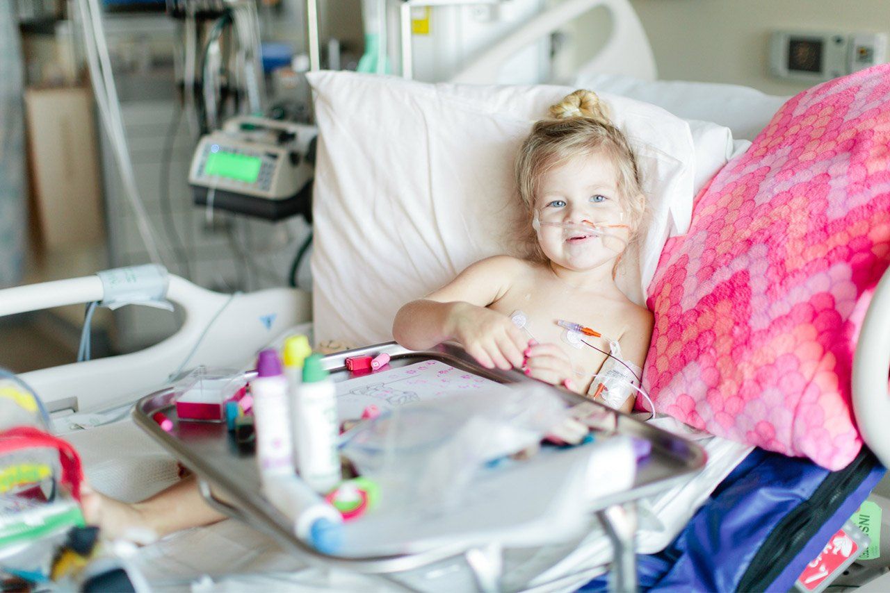 Riley sits in her hospital bed with art supples.