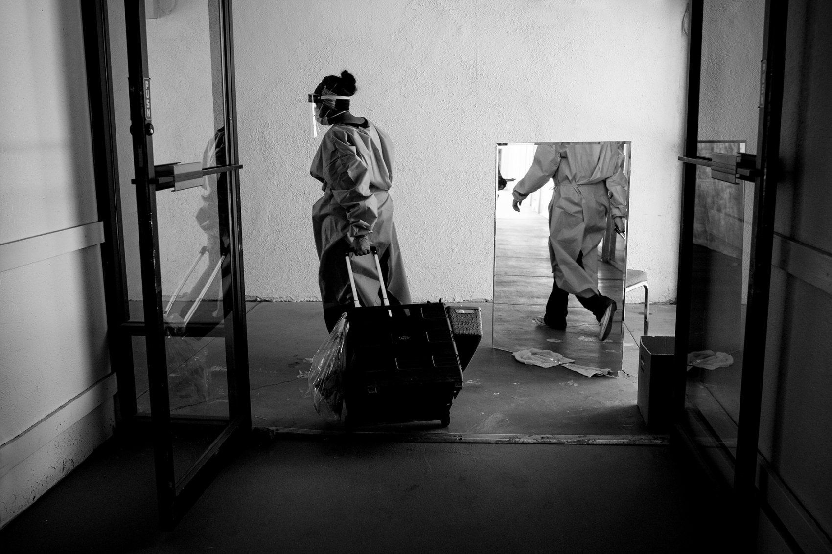 health worker rolls a bag in a hotel hallway