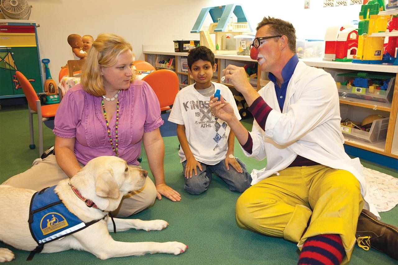 Nilani the Labrador at a children's playroom at the hospital with staff and a young patient.