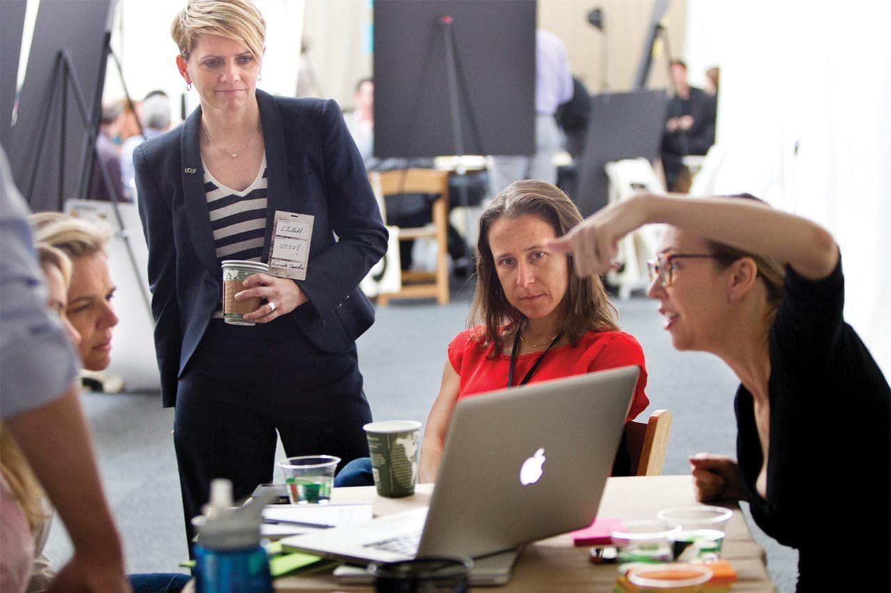 A group of people around a table with a laptop have a discussion.