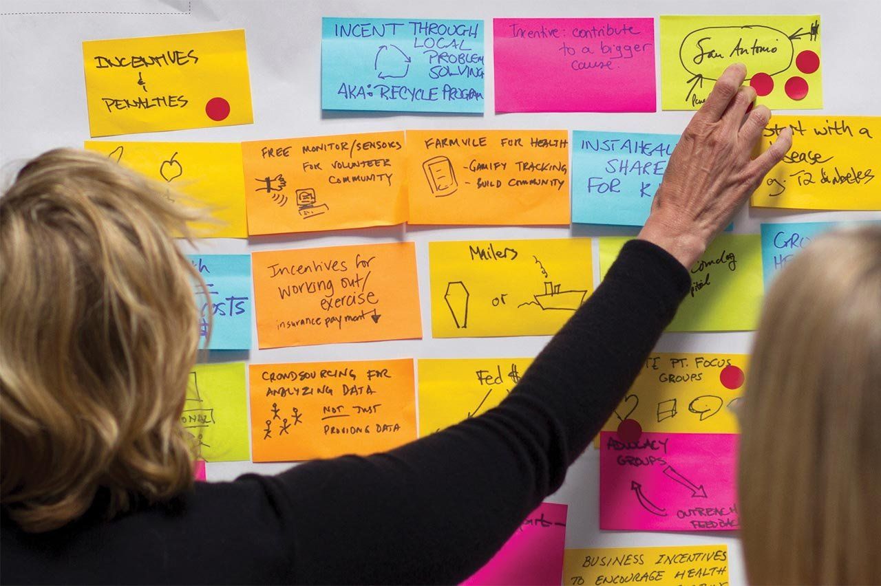 A woman points at sticky notes on a wall.