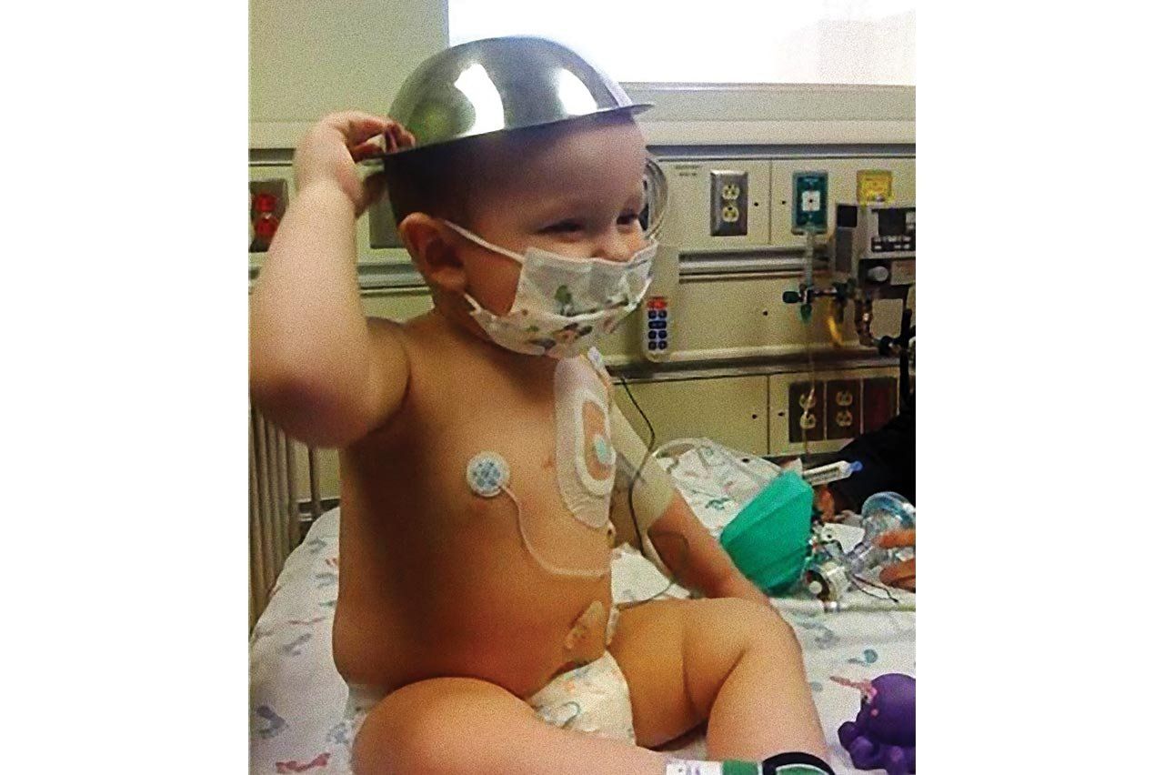 Toddler, Harry Drake, with a bowl on his head and medical devices on his chest.