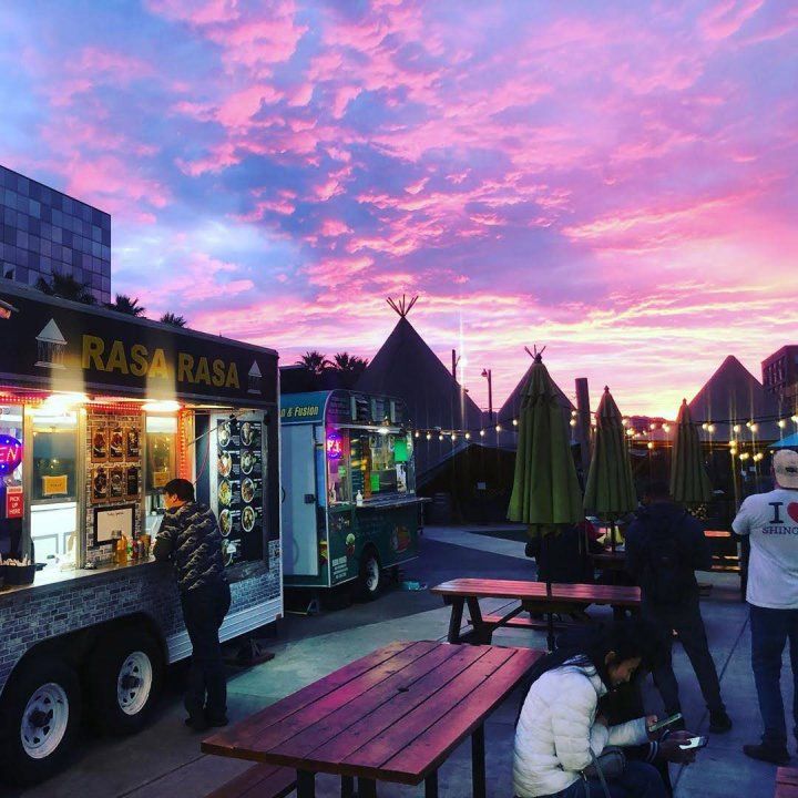 A dramatic sunset lights up picnic tables and a row of food trucks