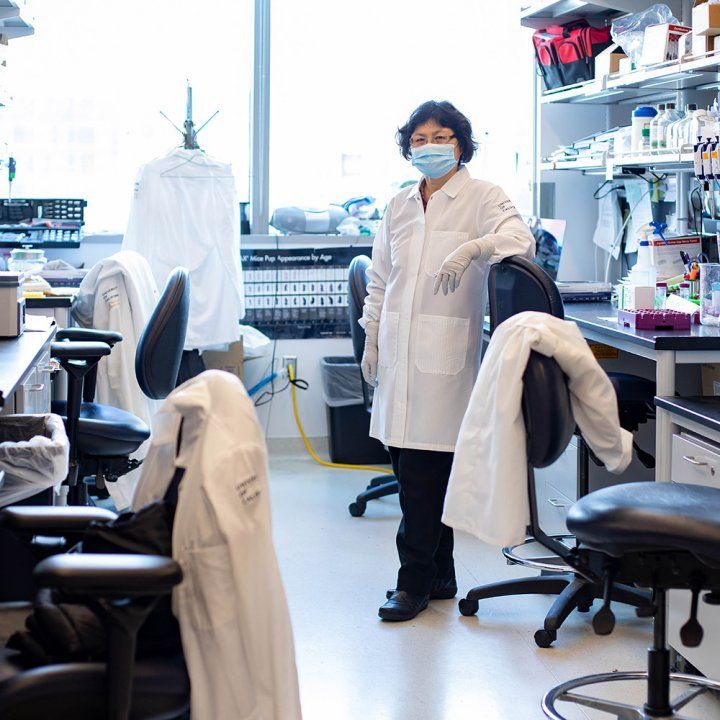 A woman wearing a white lab coat stands in her sunlit lab