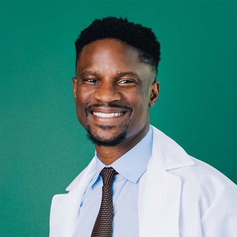 Akinyemi Oni-Orisan wearing a white lab coat and a brown tie.