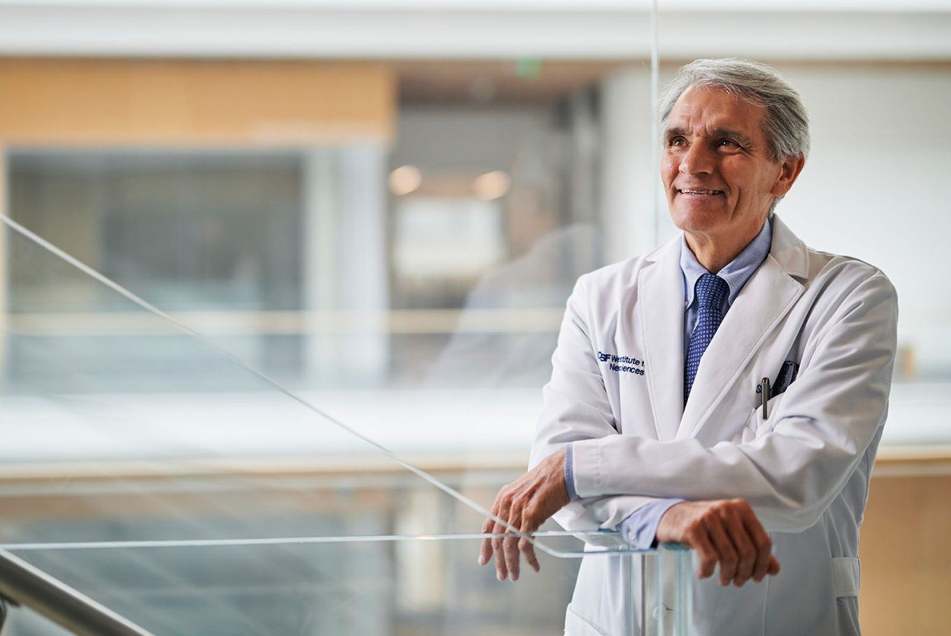 Stephen Hauser looks up and smiles in a doctor’s white coat inside the UCSF Weill Institute for Neurosciences building.