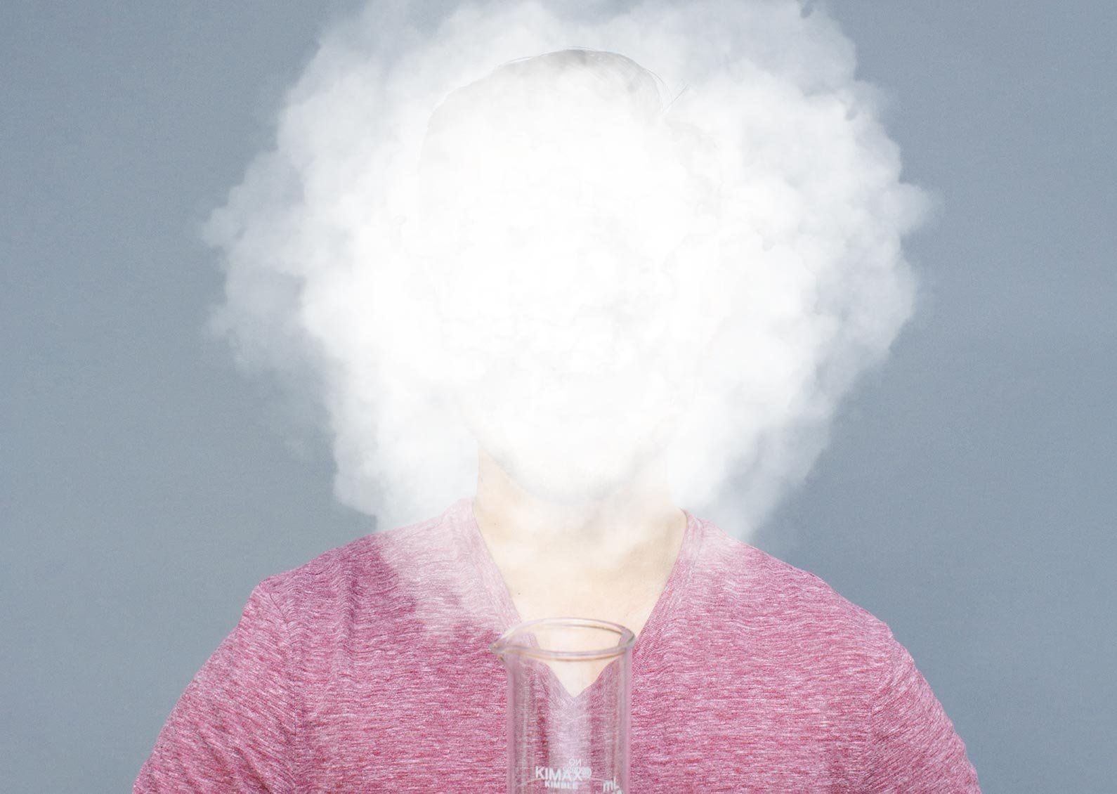 Photo of a person holding a large glass beaker, whose face is completely obscured with a smoke cloud.