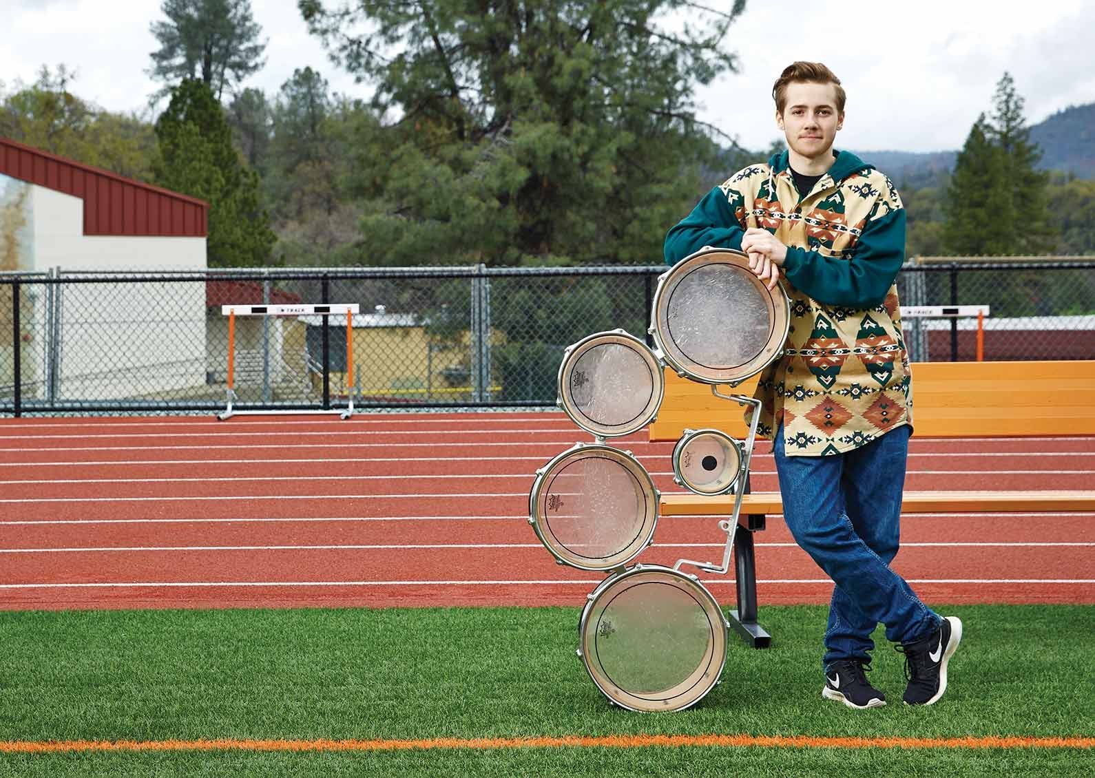 Oliver Bishop with drumline equipment at his high school track field.