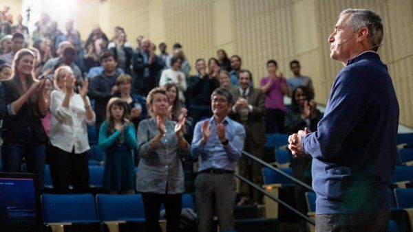 David Wofsy stands in front of a clapping audience at Cole Hall during the Last Lecture event