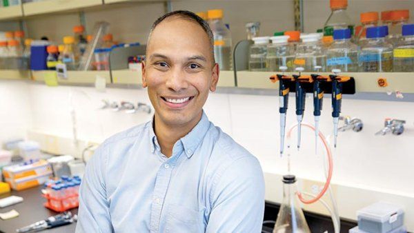 Portrait of Claudio Villanueva in a lab with equipment behind him.
