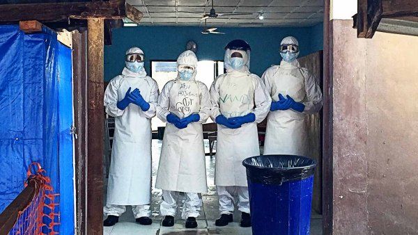Volunteers in protective gear standing within the boundaries of an Ebola isolation unit in Sierra Leone.