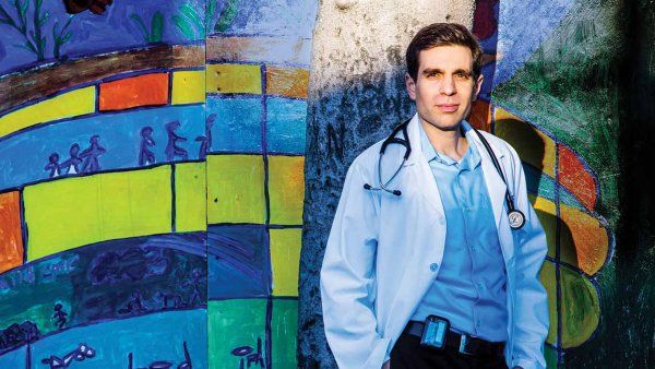Jonathan Van Nuys stands in front of a colorful mural in a lab coat with stethoscope.