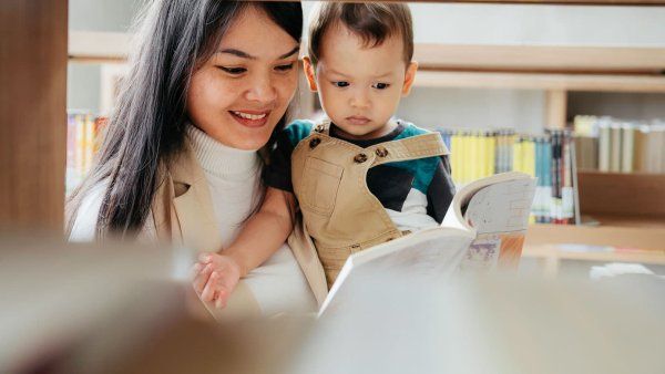A mother reads a book to her baby son at a library.