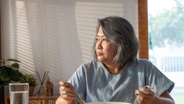 A middle-aged Asian woman eats alone at a dining table.
