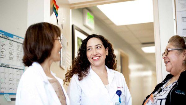 A female doctor wearing a white coat speaks with two nurses.
