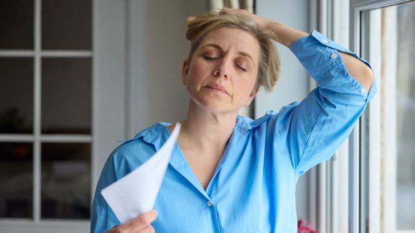 A Caucasian woman airs herself with a stack of papers and holds up her hair in order to cool down.