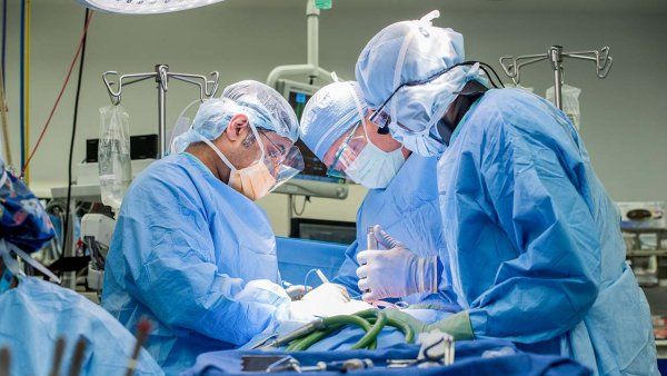 Several surgeons circle a patient in full medical gear during a cervical spine surgery operation.