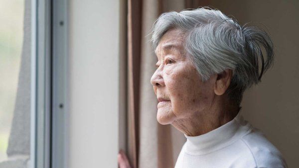 An elderly Asian woman stares wistfully out of a window.